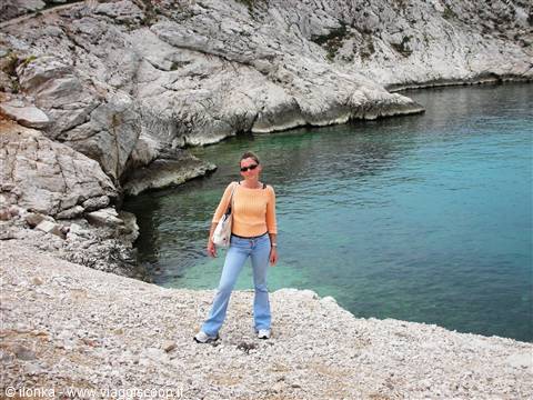 Woman in orange sweater and jeans on white rocks beside turquoise water