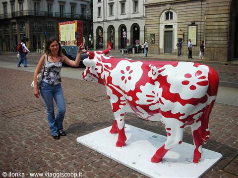 Woman petting a red and white cow sculpture in a Turin square