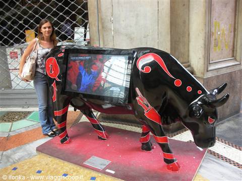 Woman beside a black and red cow sculpture with a TV screen, outdoors