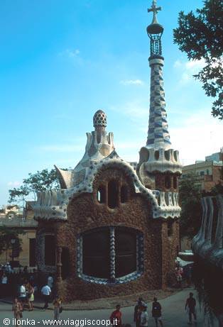 Gaudí's gatehouse at Park Güell, Barcelona: stone walls, white mosaics, cross-topped spire