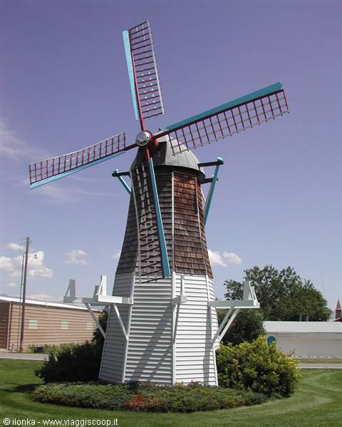 White wooden windmill with red and blue sails under clear sky