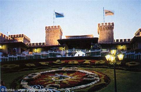 Gardaland entrance with crenellated towers, flowerbeds and flags at dusk