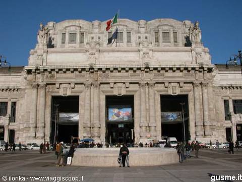 Milan Centrale station marble facade with flags under a blue sky