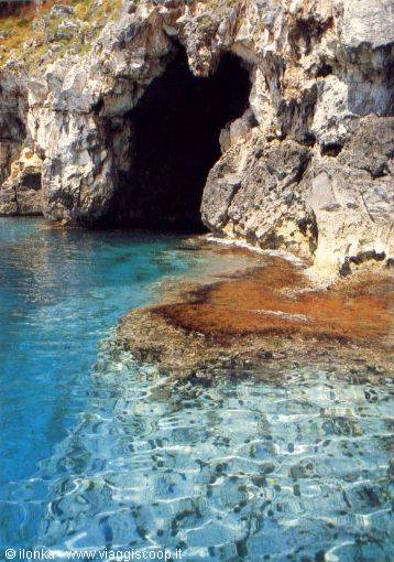 Clear turquoise water in front of a cave in limestone rock