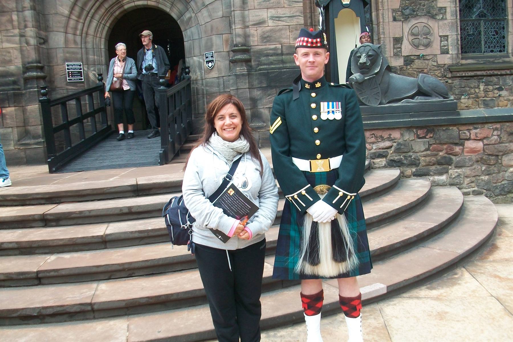 Tourist beside soldier in green kilt on stone castle steps