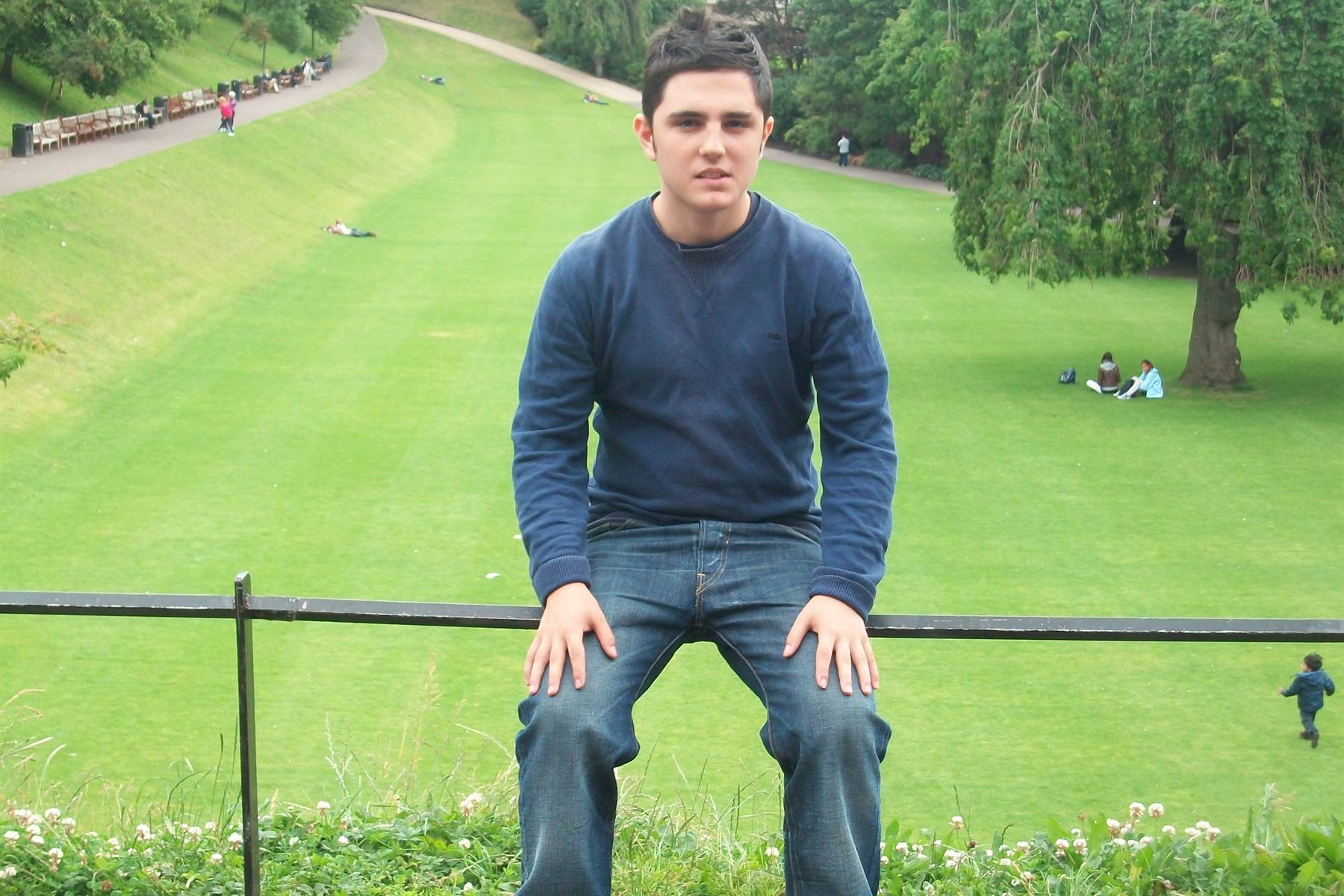 Boy sitting on an iron railing in front of a large green lawn