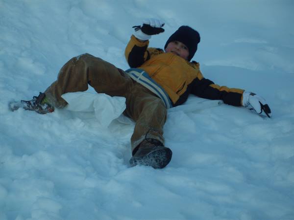 Child in yellow jacket and black hat fallen on snow with plastic sled