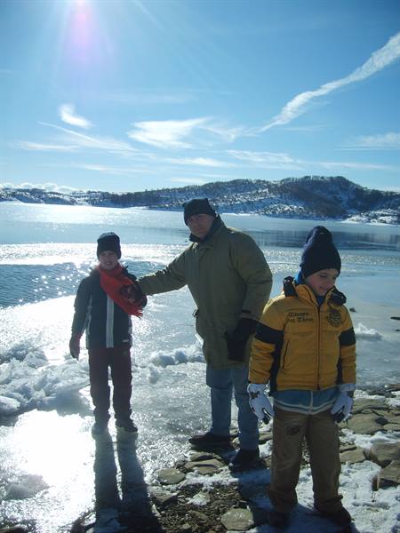 Man and two children in hats and winter jackets on frozen lakeshore