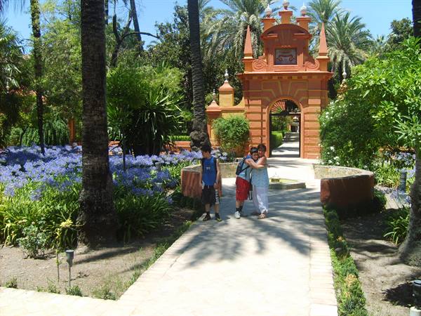 Tourists before the red portal of Seville's Alcázar among palms and agapanthus