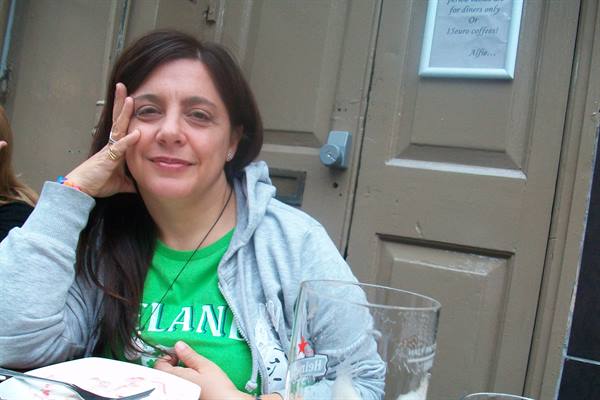 Smiling woman in grey hoodie and green shirt sitting at a table with glass