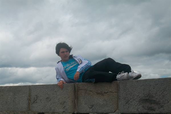 Boy lying on a granite wall under a cloudy sky