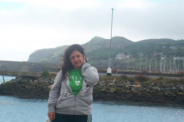Woman in grey hoodie on Bray harbour, green hills and boats behind