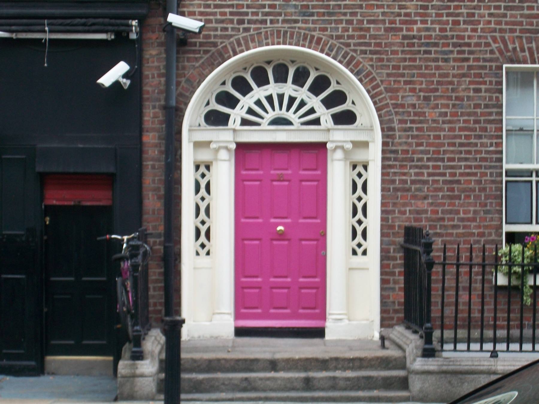 Bright pink Georgian door with white fanlight on red brick facade, Dublin