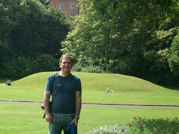 Man in blue t-shirt with shoulder bag on green lawn among trees