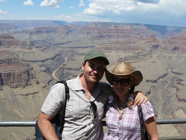Couple embracing before the Grand Canyon, the Colorado river carving red gorges below clouds