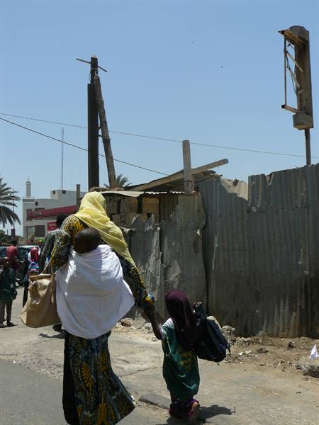 Veiled woman carrying child walking past corrugated metal shacks