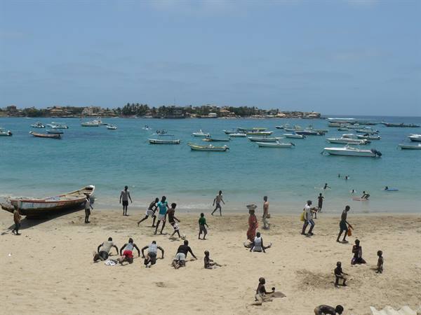 Children playing on sand, boats anchored offshore at Ngor beach