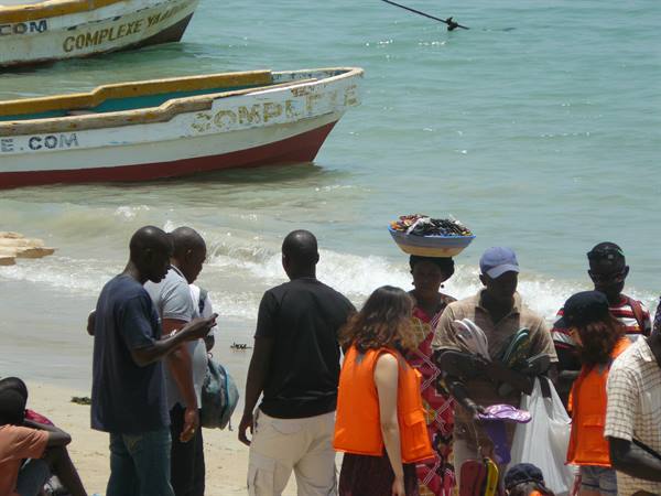 Woman carrying basket on head among fishermen and painted boats on beach