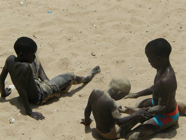 Three children covered in sand play sitting on the beach