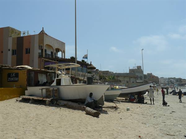 Fishing boats hauled up on the sand, fishermen working by colorful buildings