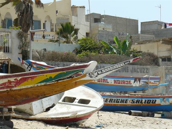 Colorful painted fishing pirogues stranded on the sand in front of houses