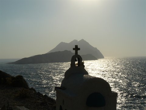 White chapel bell tower with cross above glittering sea, volcanic island behind