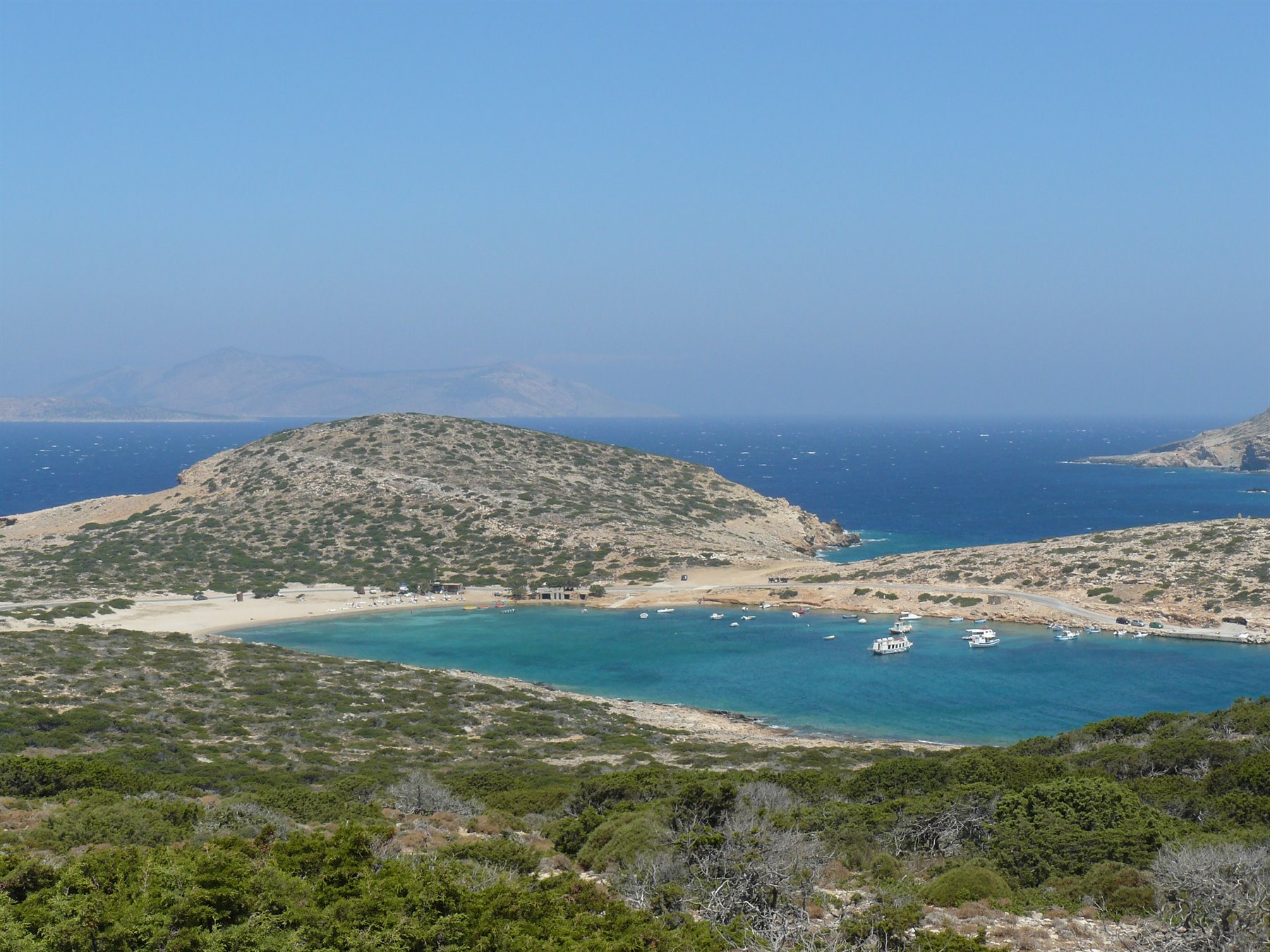 baia turchese con barche ancorate tra colline aride e macchia mediterranea