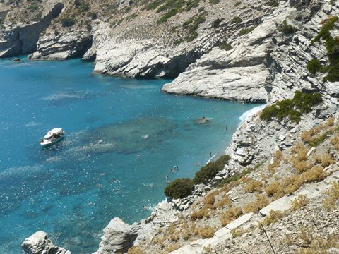 boat anchored in rocky cove, turquoise water, swimmers among the cliffs