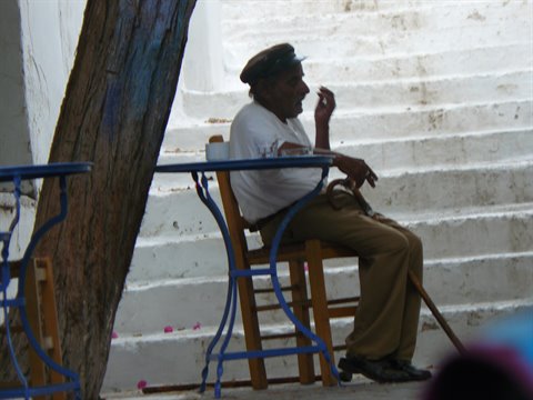 Elderly man in cap sitting by blue tables on white steps