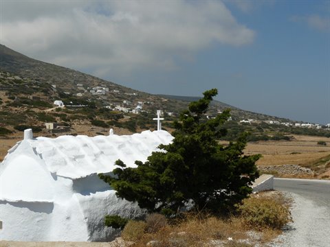 Whitewashed chapel with cross beside a juniper tree on a rural road