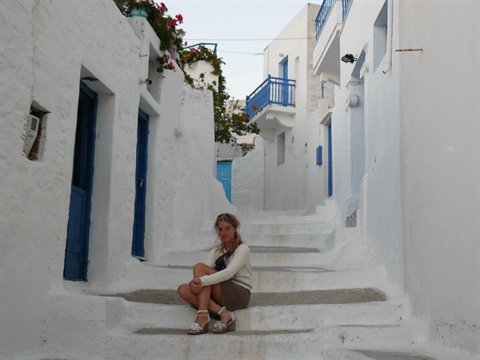 Woman sitting on steps of a Cycladic alley with whitewashed houses and blue doors