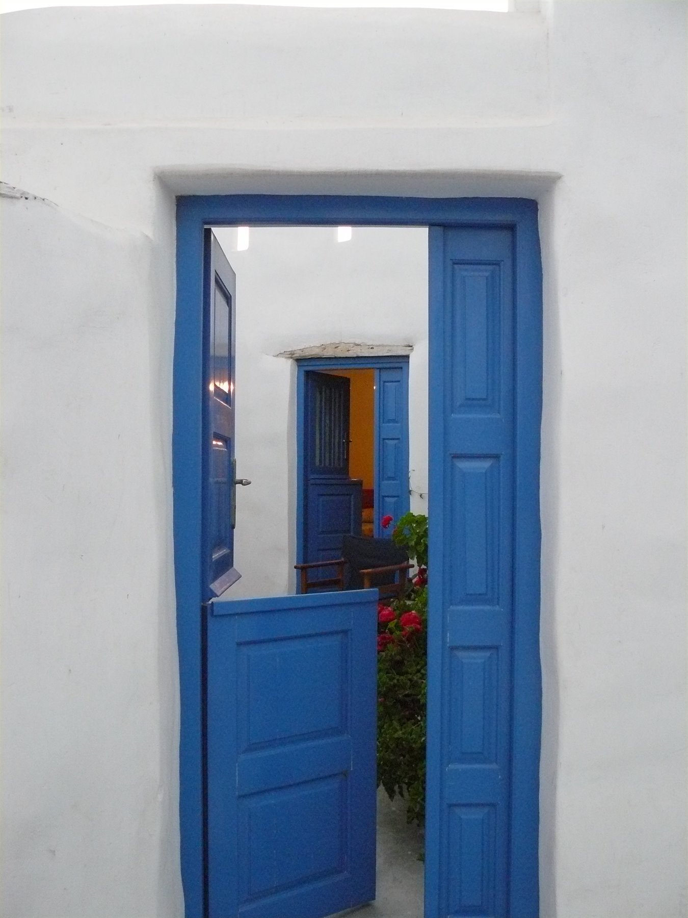 Porta blu a metà aperta su muro bianco a calce, fiori rossi