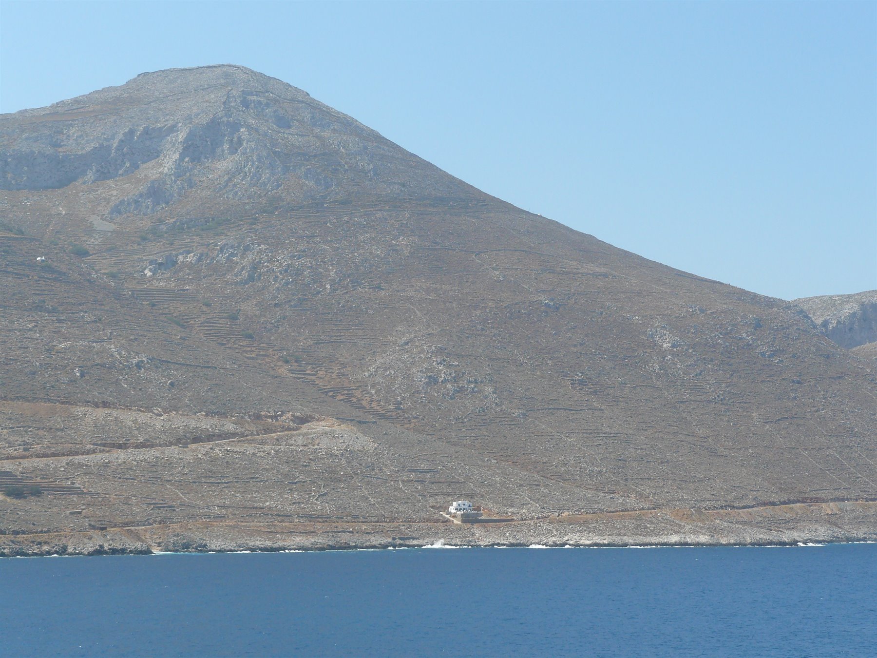 Monte arido e roccioso sopra il mare blu, una piccola casa bianca sulla riva