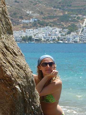Woman with headscarf and sunglasses beside a rock, turquoise sea and white village