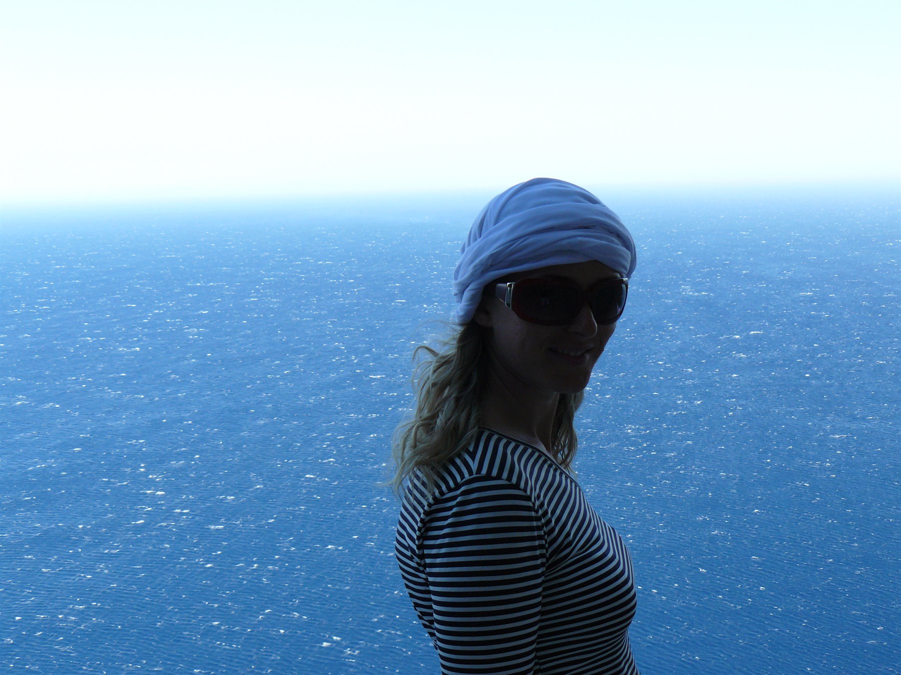 Donna con bandana azzurra e maglia a righe davanti al mare