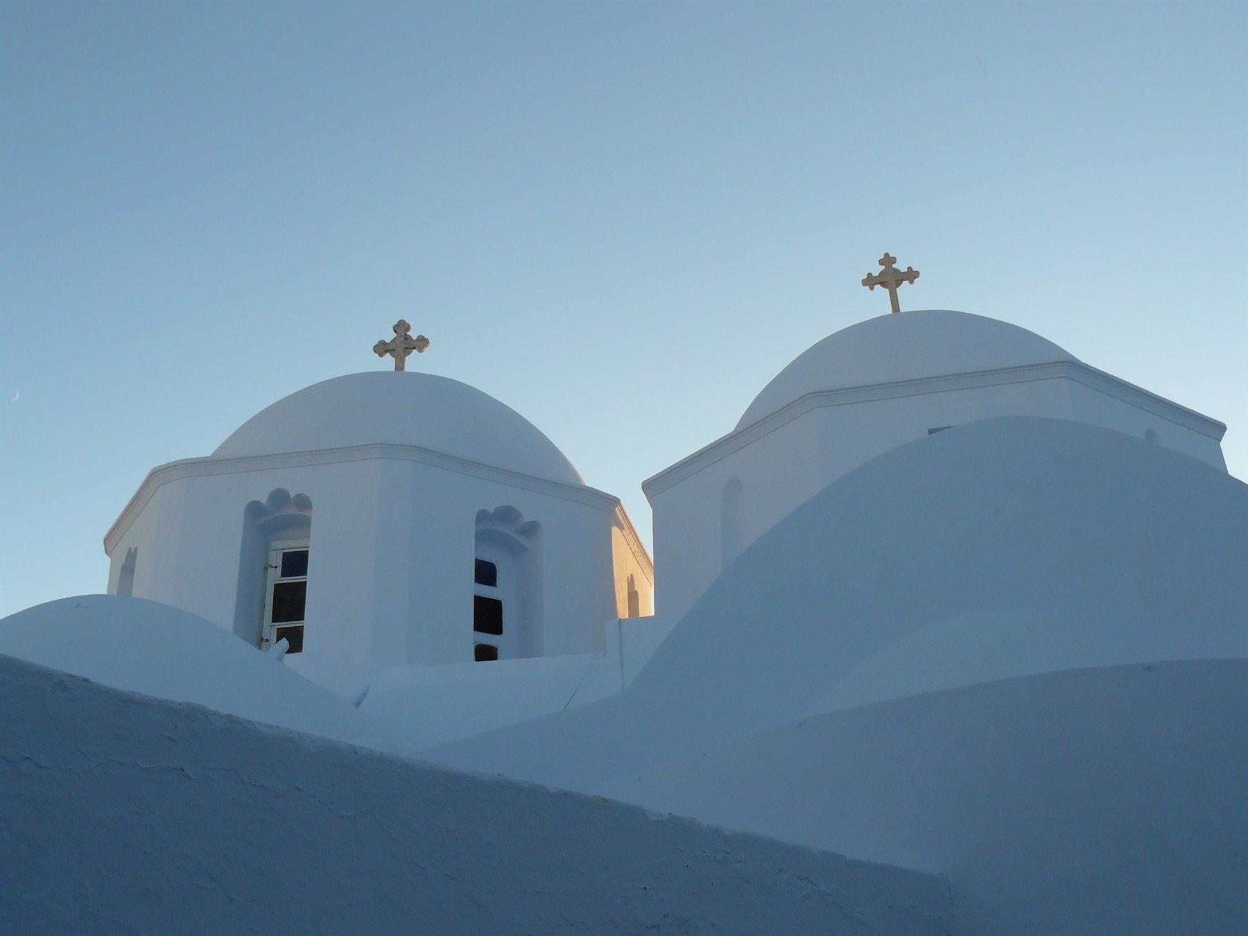 Due cupole bianche con croci dorate, chiesa cicladica sotto cielo azzurro