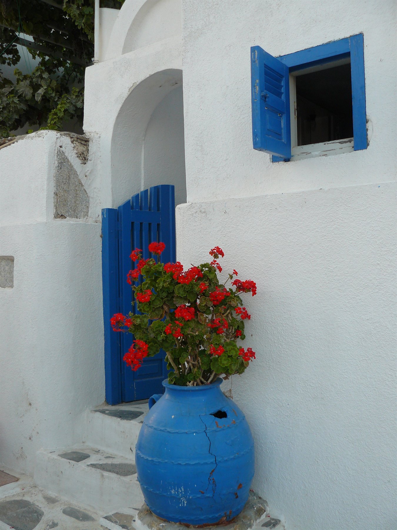 Casa bianca con porta e finestra azzurre, gerani rossi in anfora blu