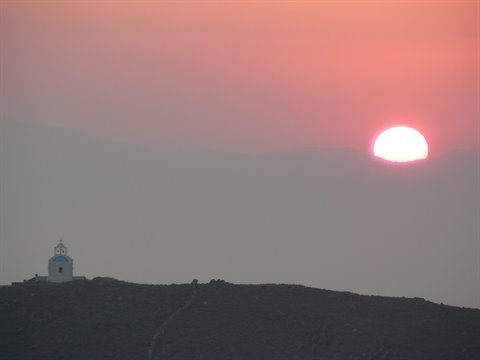 Red sun rising over dark hill, small white church with bell tower