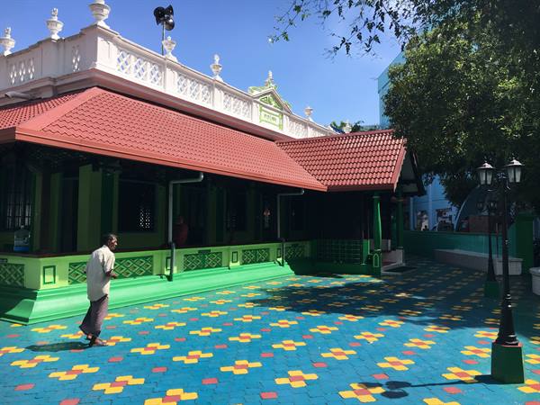 man walks across the colorful tiled courtyard of a green mosque