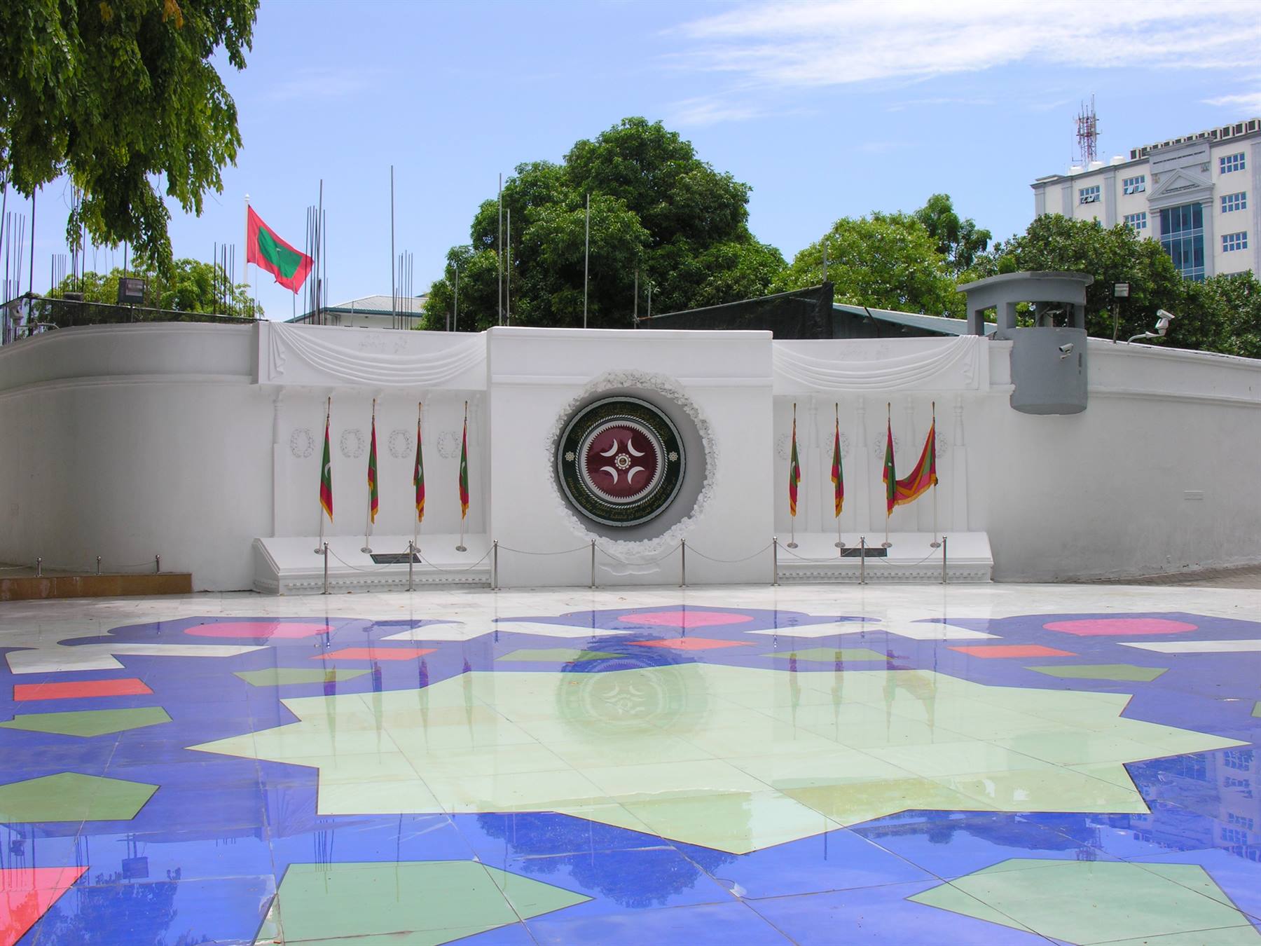 Monumento bianco con bandiere a Malé, pavimento a mosaico blu e verde sotto il sole
