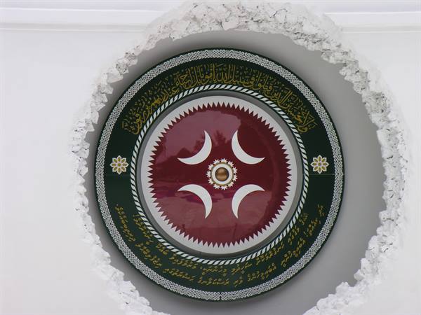 Round medallion with red crescents and Arabic calligraphy on carved white wall