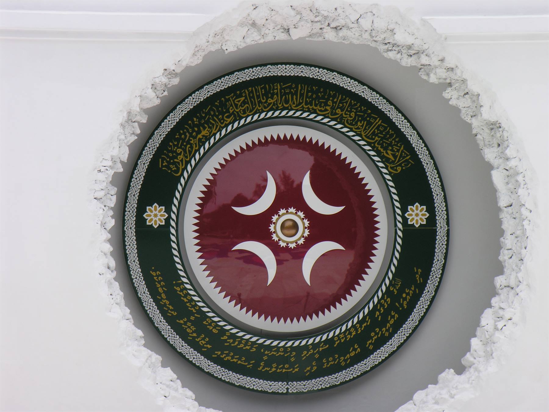 Medaglione rotondo con mezzelune rosse e calligrafia araba su muro bianco intagliato