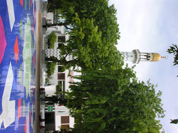 White minaret with golden dome among green trees, colorful mosaic tiled courtyard