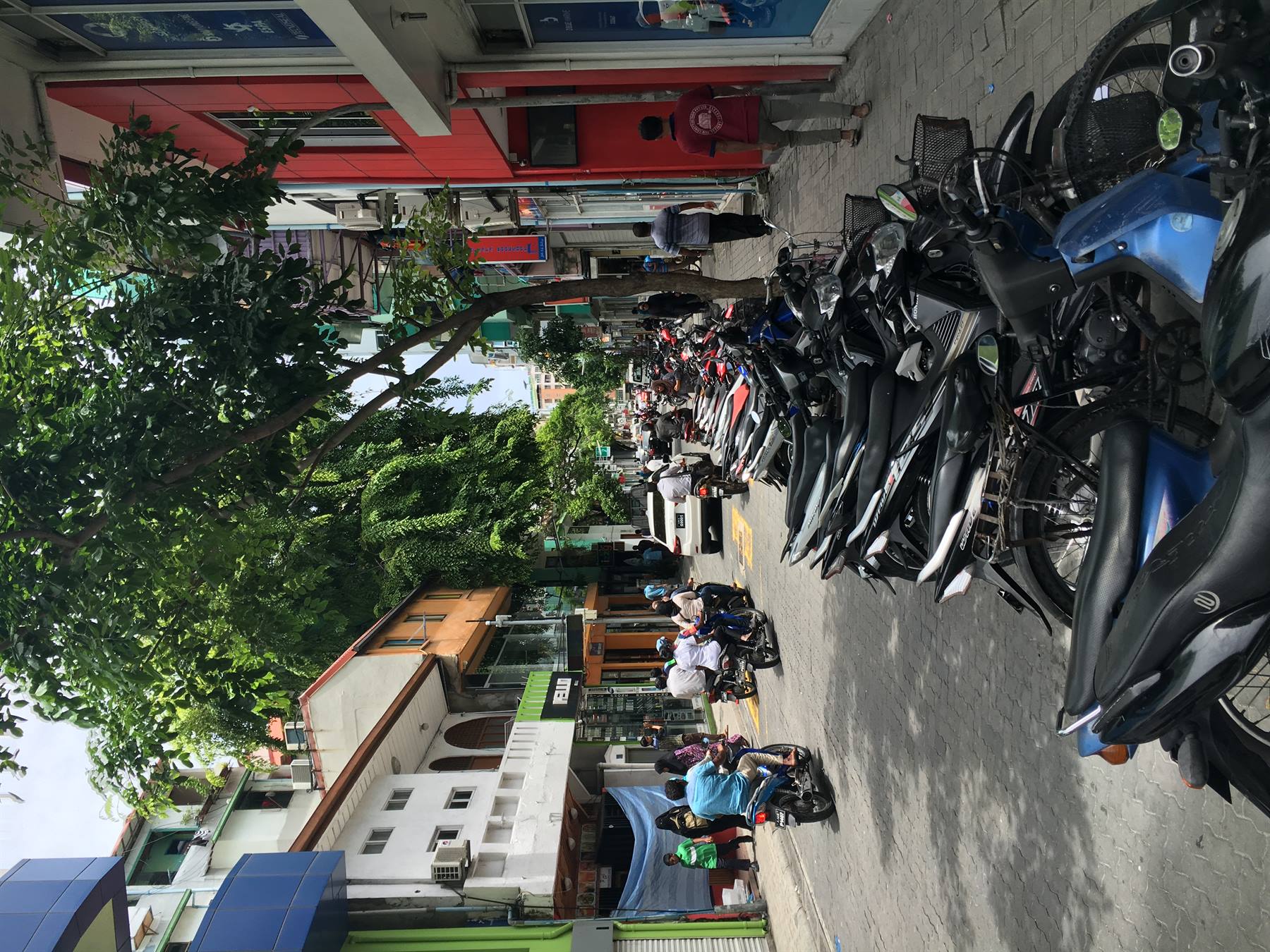 Moto in fila sul marciapiede davanti ai negozi, gente cammina