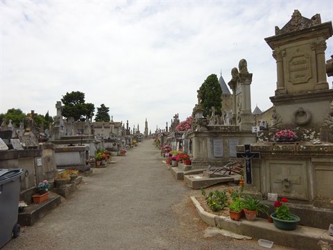 Gravel path lined with stone tombs, flowers and crosses in a French cemetery