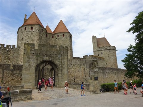 Tourists walking by medieval stone walls and conical towers of Carcassonne