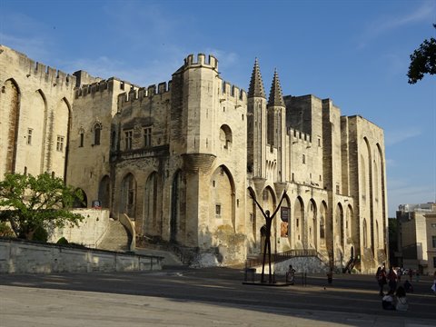 Papal Palace of Avignon, pale stone walls, tourists in the sunny square