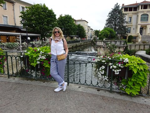 Smiling woman leaning on flowered railing beside a canal, L'Isle-sur-la-Sorgue
