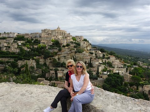 Two women sitting on a rock in front of the hilltop village of Gordes