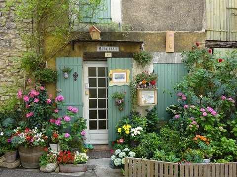 Stone house with glazed door, green shutters and colorful flowers, Mireille sign